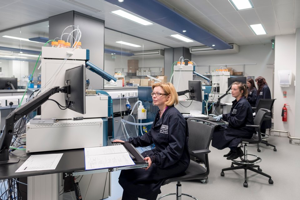 People sat in a lab space in navy blue overalls working on lab computers