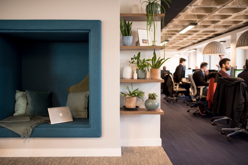 Office space with a comfy seating section in the center surrounded by people sat a office desks working on laptops