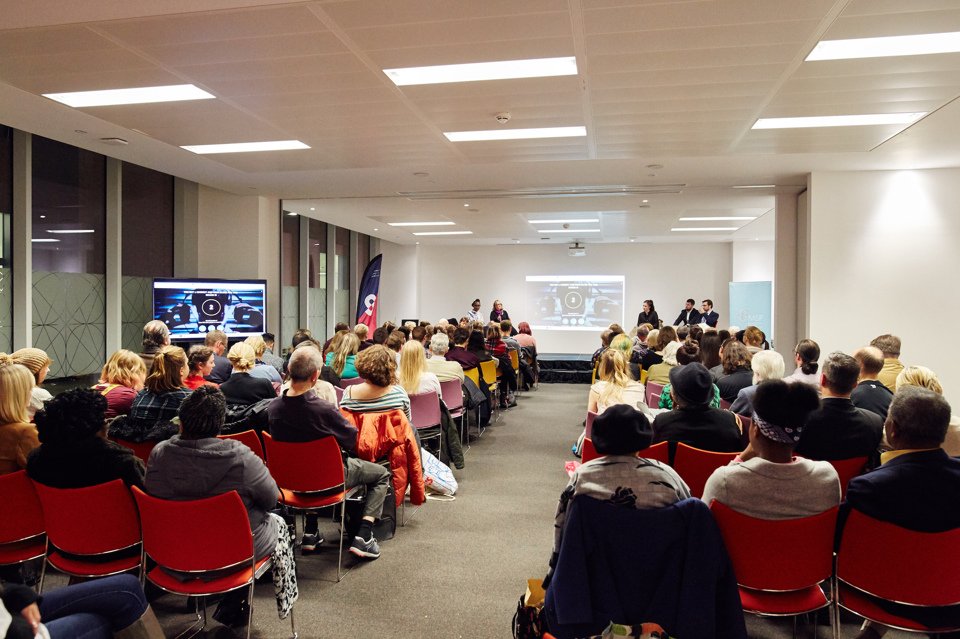 Overview of a conference with 2 groups of people sat watching