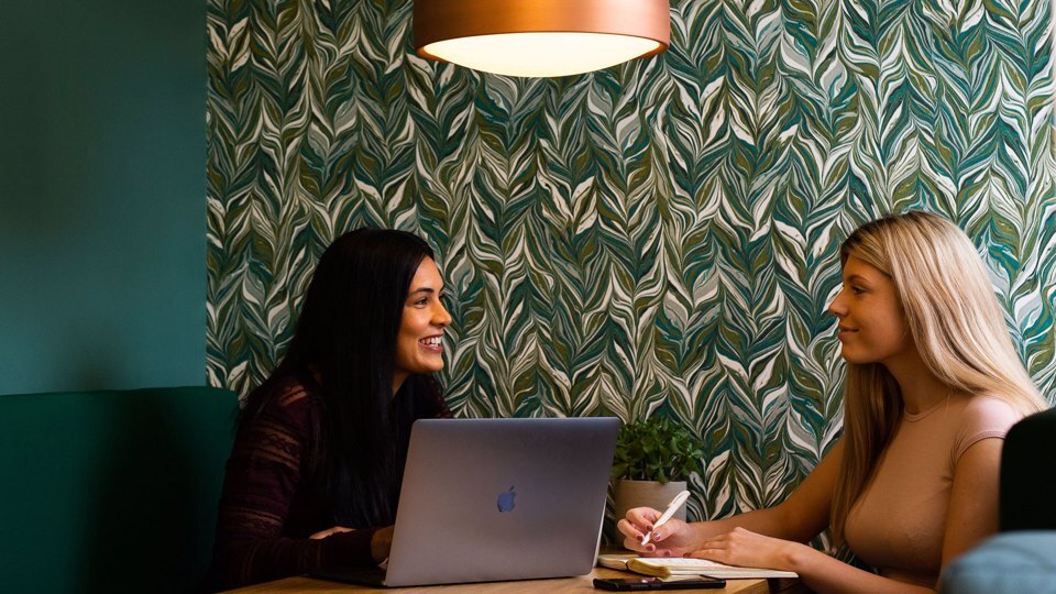 2 people sat at a desk collaborating in a breakout space