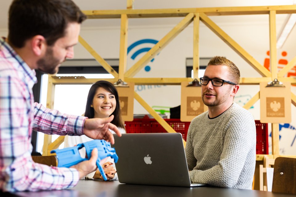 The Barclays Eagle lab team sat talking around a laptop whilst a man holds a robotic hand