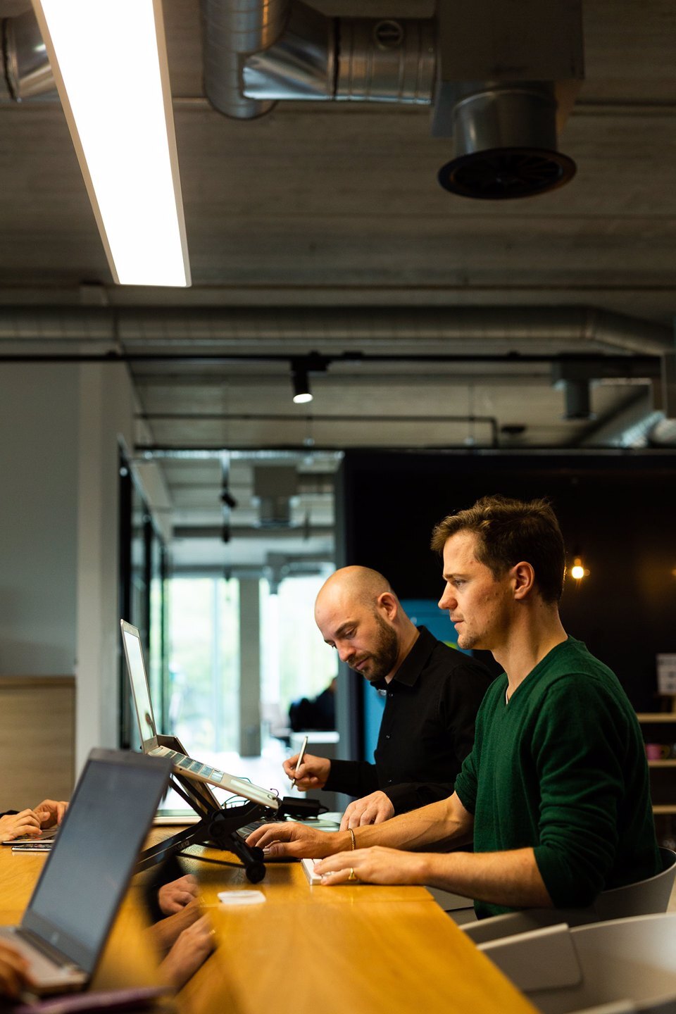 Group of people sat around a bright communal space working on laptops