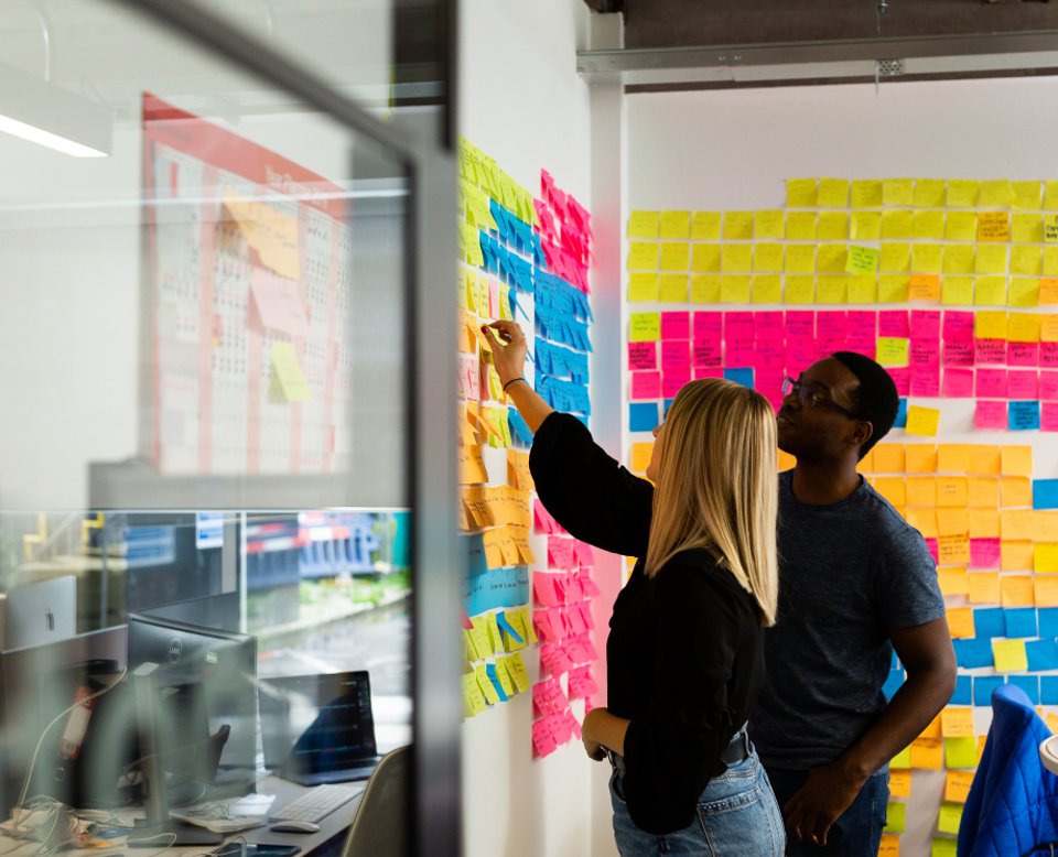 2 people having a discussion and placing sticky notes on a wall full of other notes