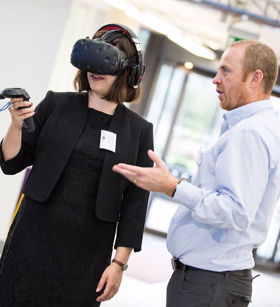 A man demonstrating to a woman wearing a VR headset