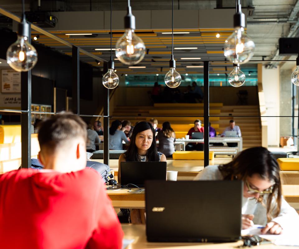 Group of people sat around a bright communal space working on laptops