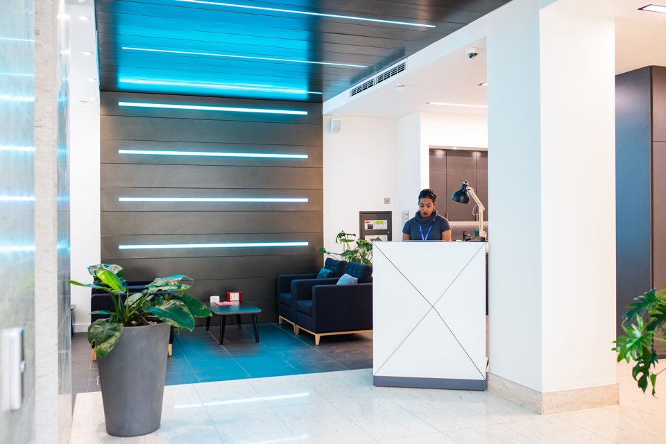 White themed reception area with comfy seating, blue striped lights on the back wall and celing and a lady stood at the reception desk