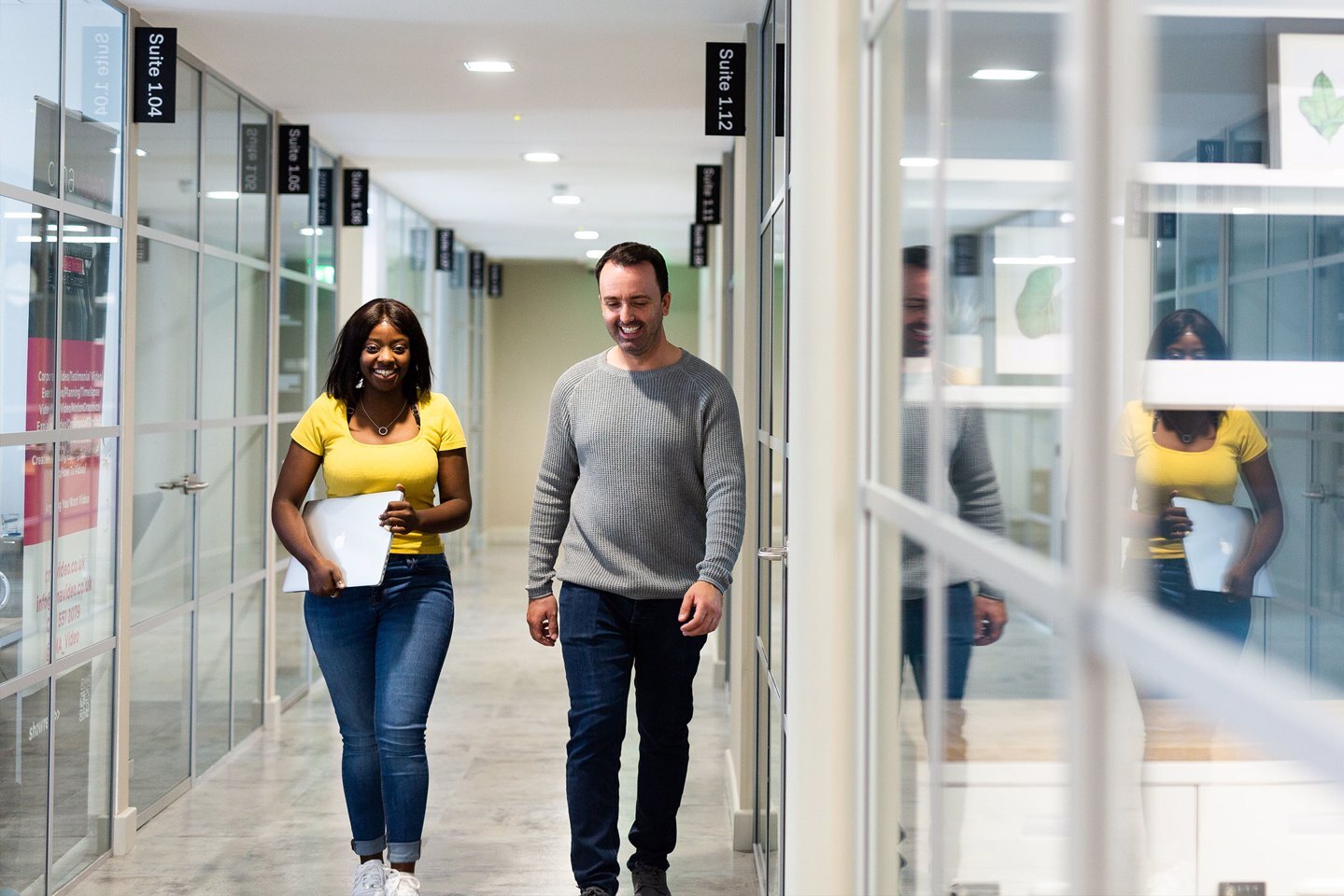 A man and a woman smiling and having a conversation while walking down a corridor