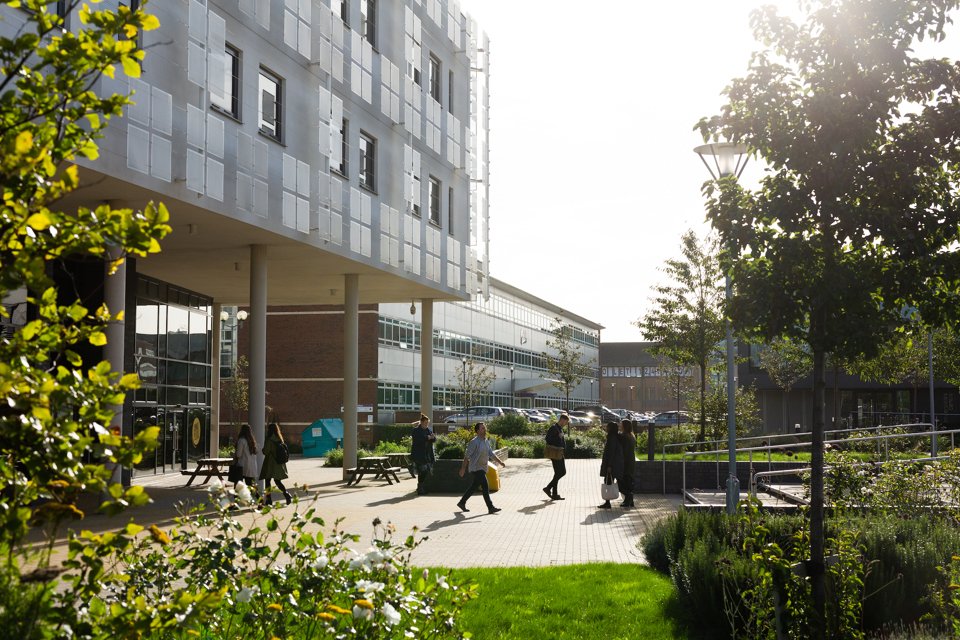 People leaving and entering the Innovation Birmingham campus through the tall, pillared entrance.