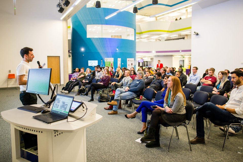 A large group of people sat down in the Innovation Birmingham event space listening to a man talking at the front
