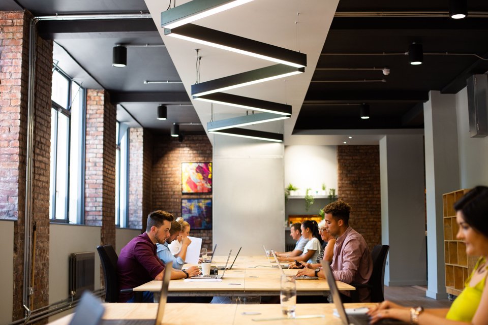 A contemporary office space with large ceiling-to-floor windows, potted plants on shelves, a painting of a plant and modern seating