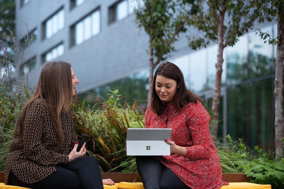 Two women sat outside the Manchester Science Park working on a laptop