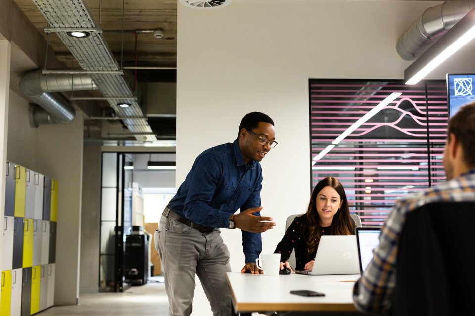 A male stood up speaking to a female who is sat at her office desk