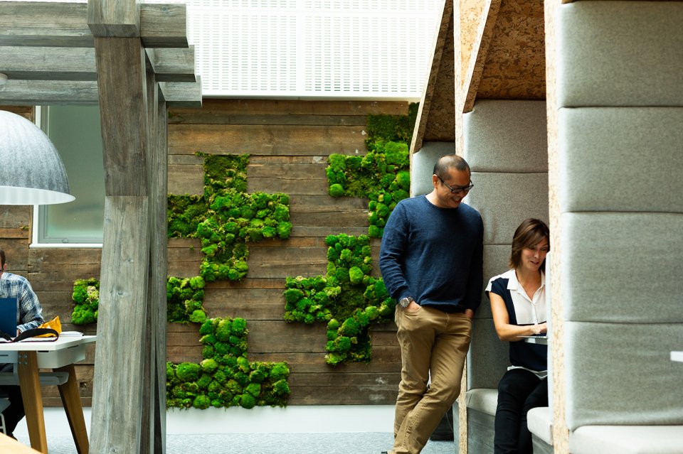 A man standing and smiling whilst talking to a woman who is sat in an urban garden meeting space