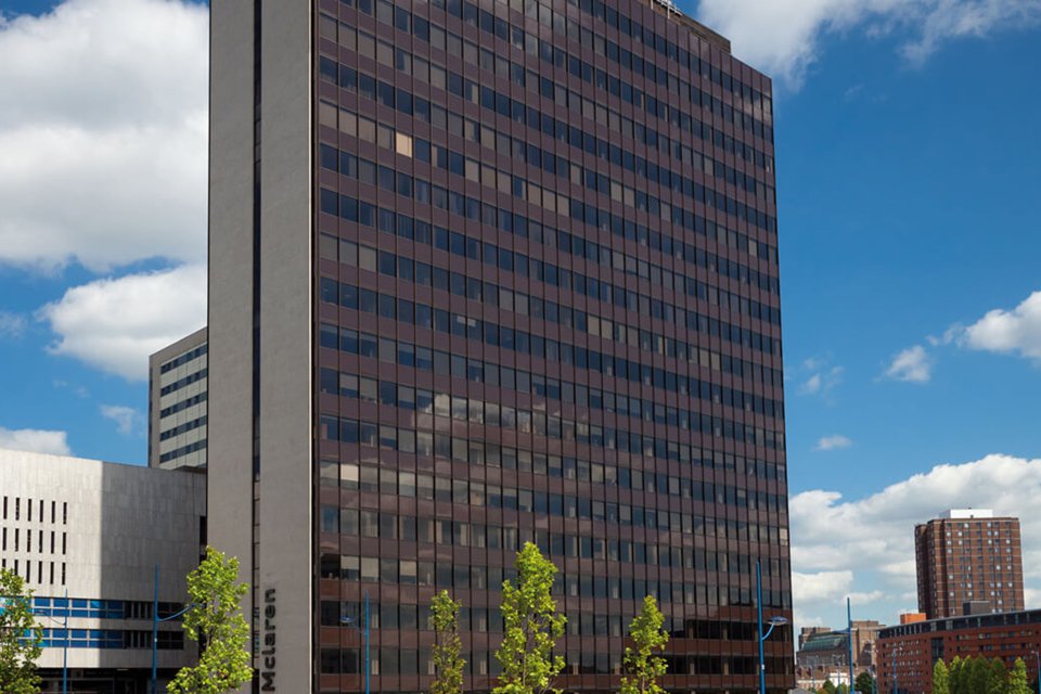 Outside look at the skyscraper like mclaren building surrounded by smaller buildings and some tress