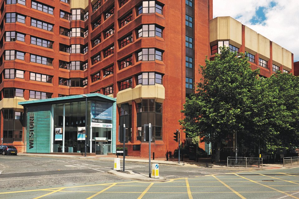 Outside look at the front of the west one building, situated next to a main road and some trees