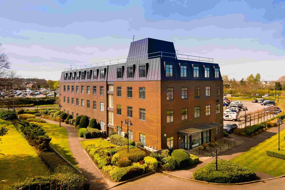 Outside look at the wilderspool park building surrounded by greenary and a car park