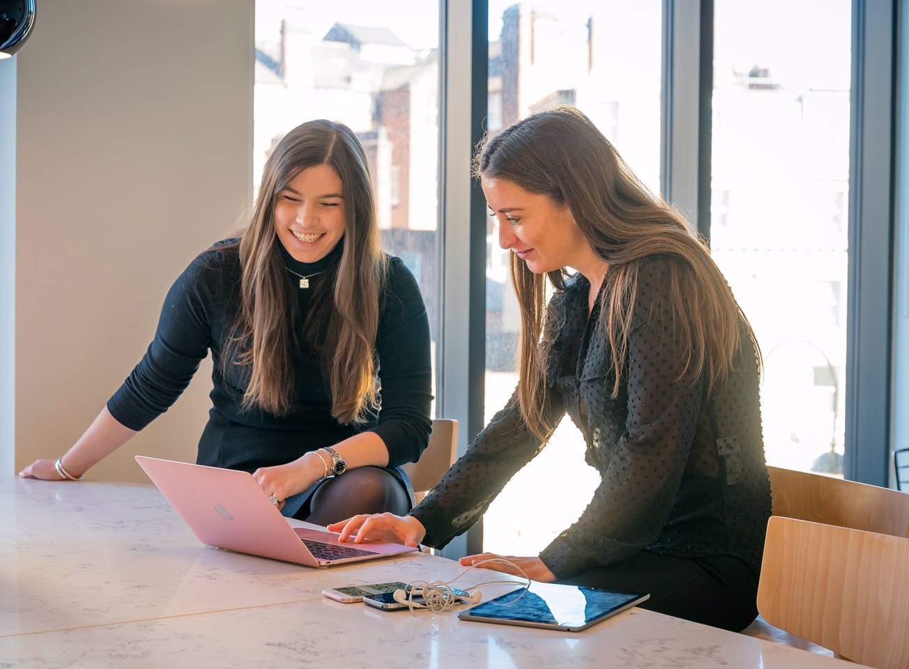 Man and a woman sat at a desk outside smiling while working on a laptop