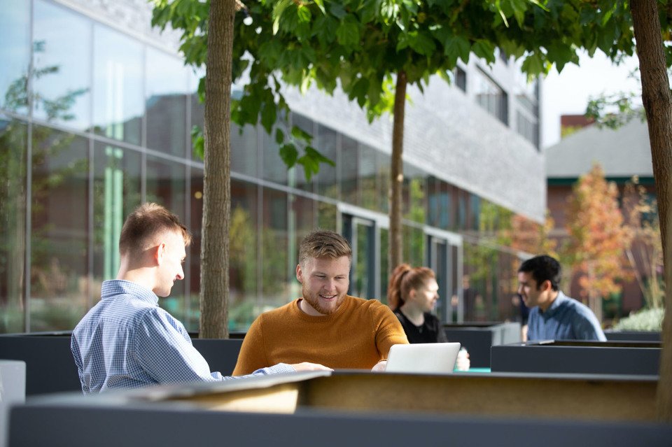 Two men sat down, working on a laptop outside the manchester science park